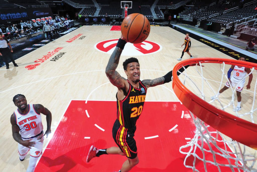 A basketball player in a Hawks jersey dunks the ball while defenders watch in Atlanta, Georgia.