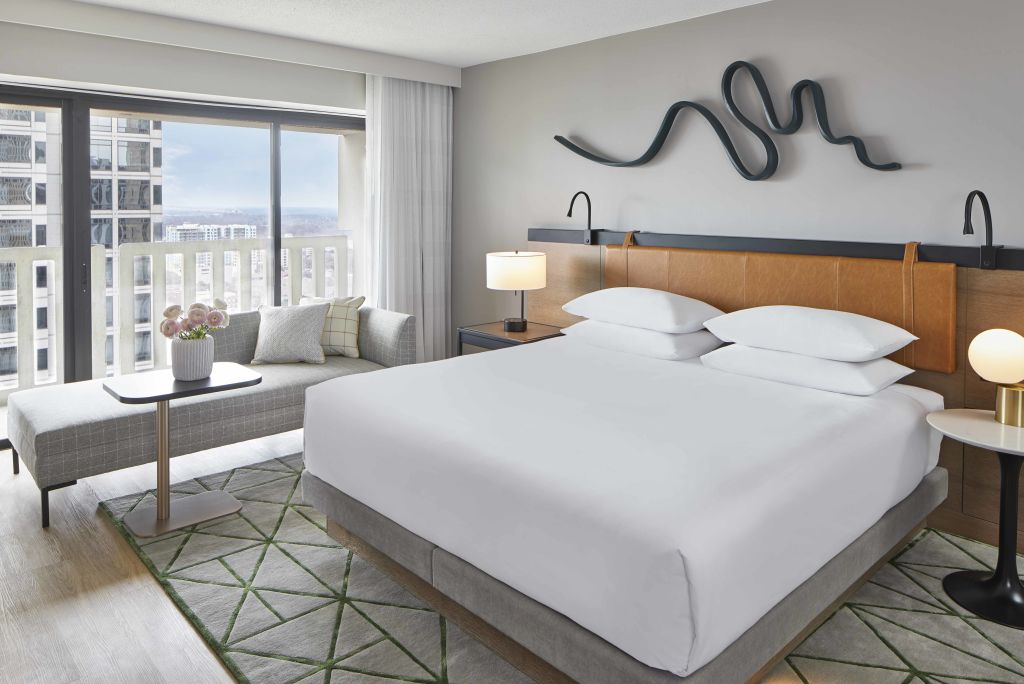 Modern hotel room with floor-to-ceiling windows, king bed, and city view in Atlanta, Georgia.