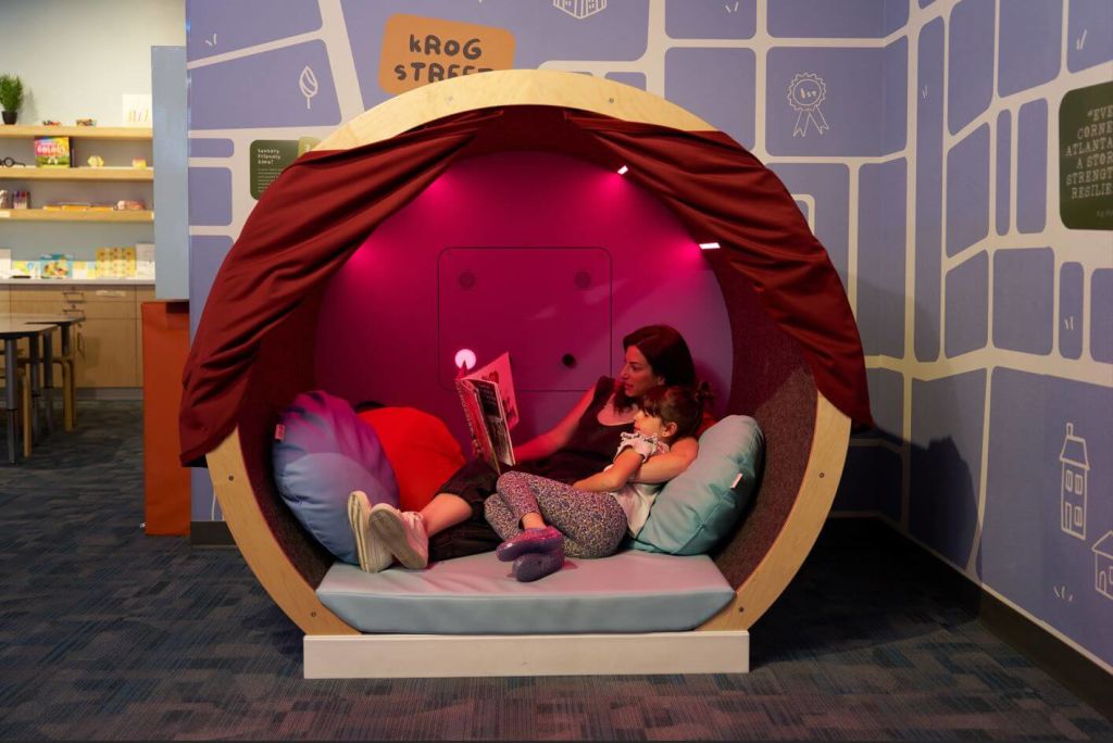 A mother and daughter are reading together in a cozy, circular reading nook with a red curtain in Atlanta, Georgia.
