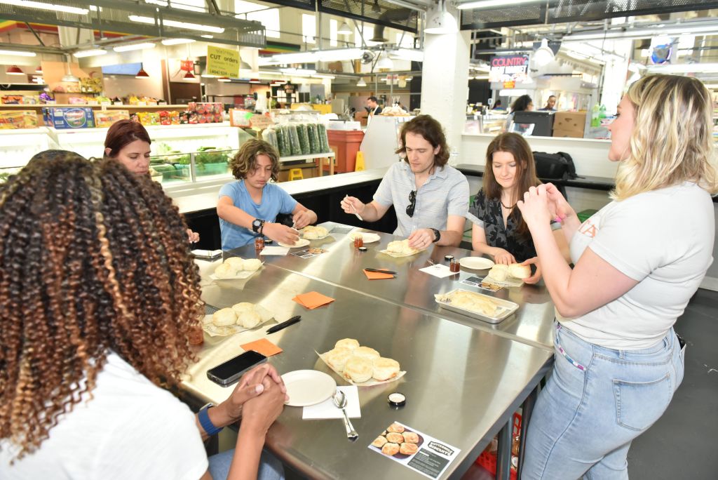 A diverse group of people are gathered around a table in a bustling market, enjoying a meal together and engaging in conversation in Atlanta, Georgia.