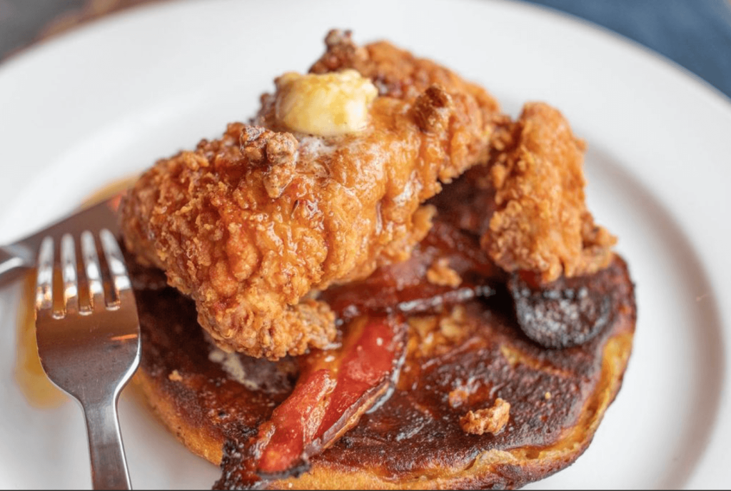 A mouthwatering stack of pancakes topped with crispy fried chicken, drizzled with syrup, and garnished with a pat of melting butter in Atlanta, Georgia.