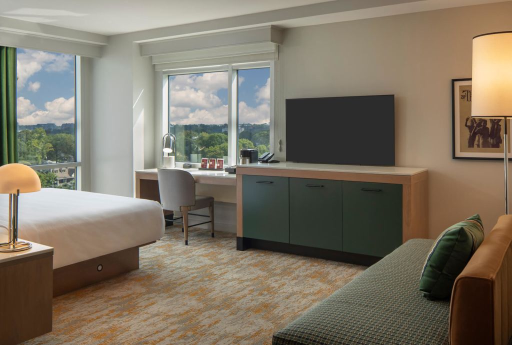 A modern hotel room with a king bed, green dresser, and large windows overlooking a cityscape in Atlanta, Georgia.