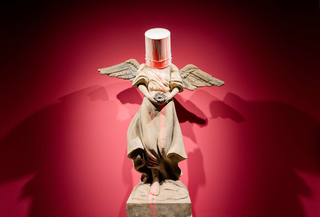 A statue of an angel with a paint can for a head, standing against a red background in Atlanta, Georgia.
