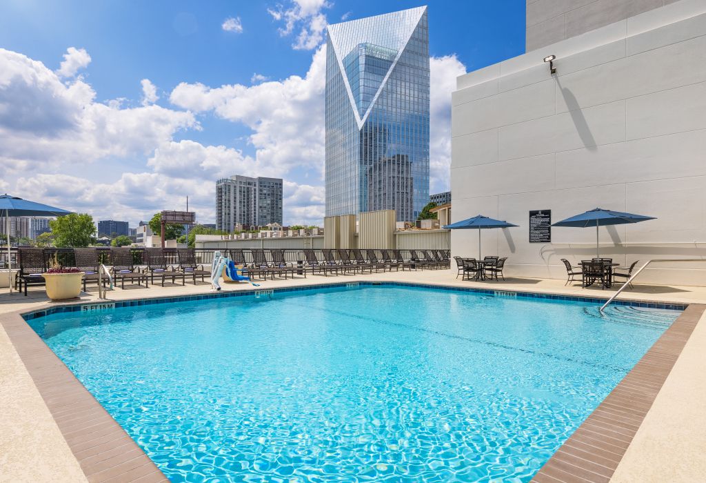 A rooftop pool with blue water, surrounded by lounge chairs and umbrellas, with a city skyline in the background in Atlanta, Georgia.