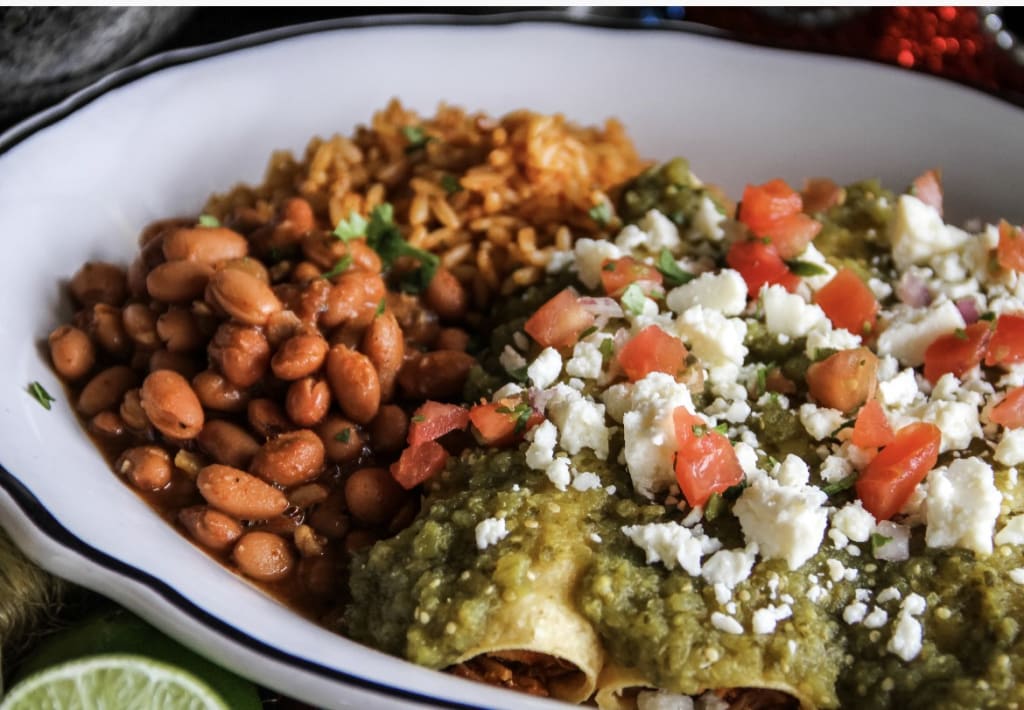 A plate of Mexican food featuring rice, beans, and enchiladas topped with salsa verde and cheese in Atlanta, Georgia.
