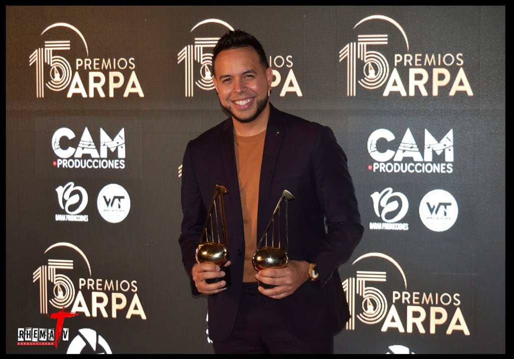A man in a suit holds two golden trophy awards in front of a backdrop in Atlanta, Georgia.