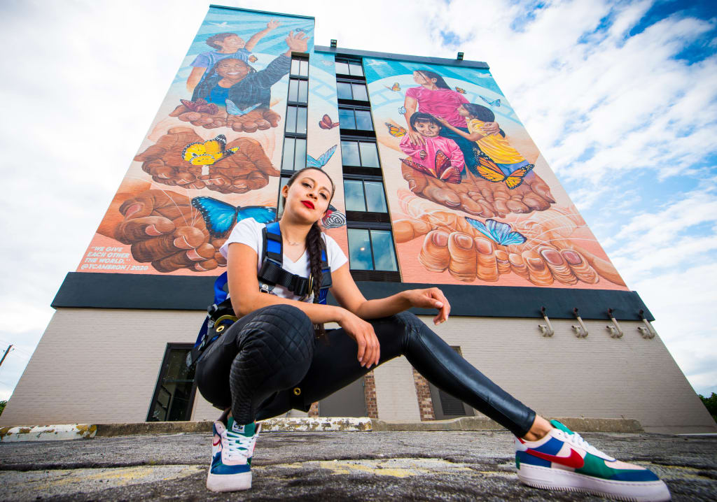 Woman in athletic gear poses in front of a vibrant mural depicting hands, butterflies, and people in Atlanta, Georgia.