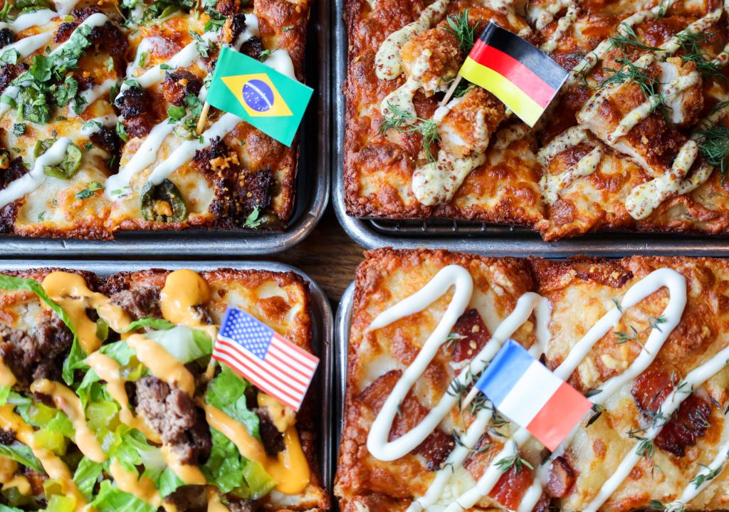Four square pizzas topped with various ingredients and decorated with small national flags in Atlanta, Georgia.