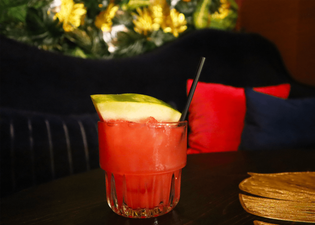 A vibrant red cocktail garnished with a watermelon wedge sits on a dark table in Atlanta, Georgia.