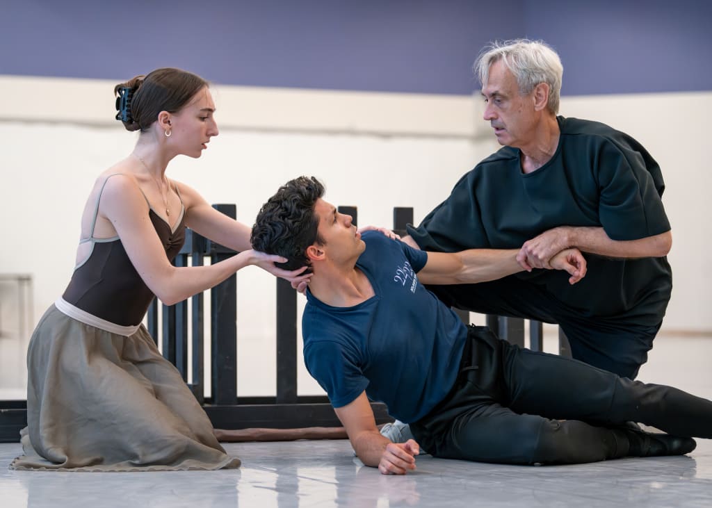Three dancers in a ballet studio, with one male dancer on the floor and two female dancers assisting him in Atlanta, Georgia.