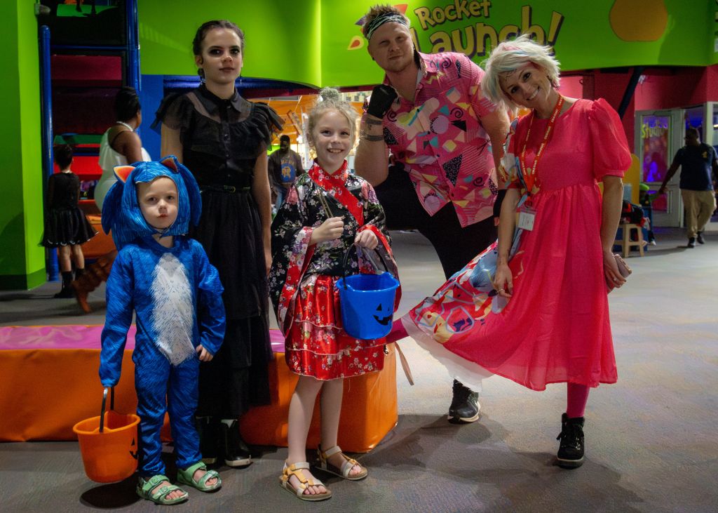 A family of five dressed in colorful Halloween costumes poses together in a vibrant indoor play area in Atlanta, Georgia.