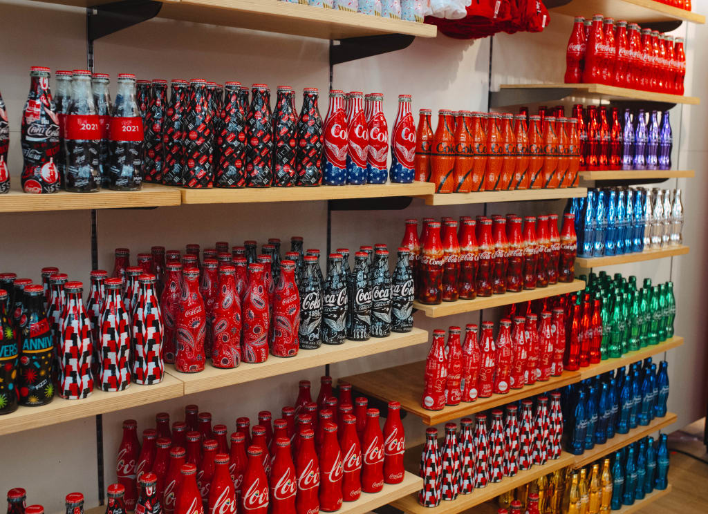 A display of colorful, limited-edition Coca-Cola bottles on wooden shelves in Atlanta, Georgia.