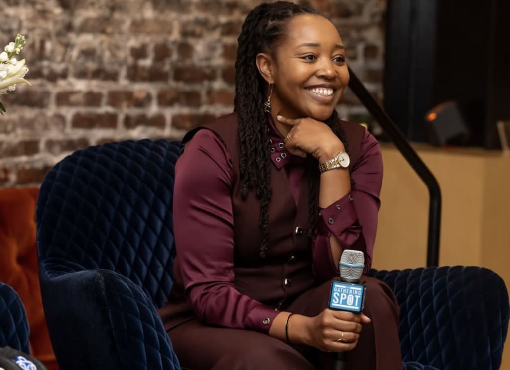 A woman with long braids sits in a blue chair holding a microphone in Atlanta, Georgia.