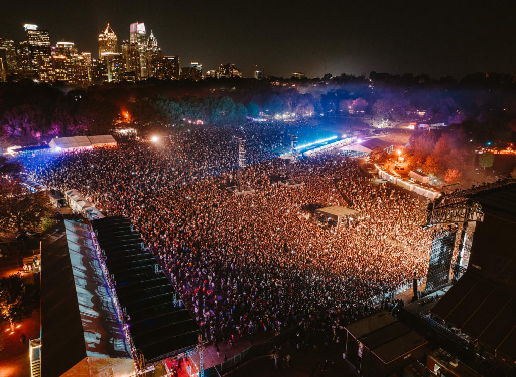 Aerial view of a massive outdoor concert with a sea of people and bright stage lights in Atlanta, Georgia.
