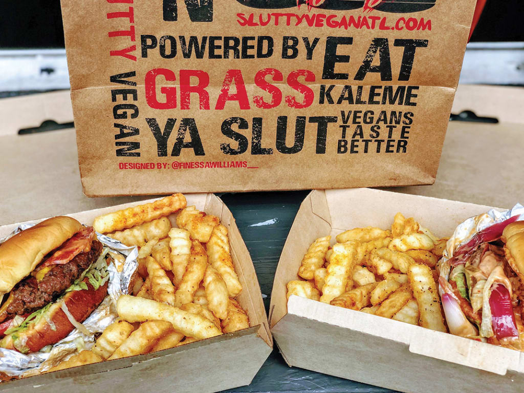 Two boxes of vegan burgers with fries, one wrapped in foil, and a branded paper bag in Atlanta, Georgia.
