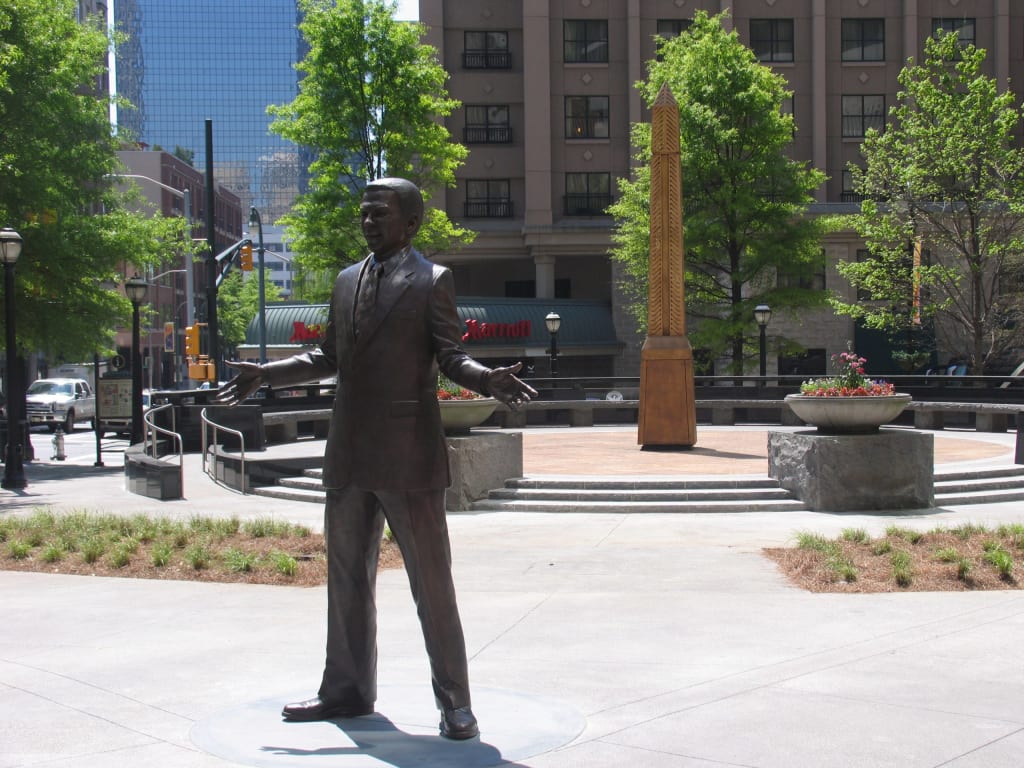 A bronze statue of a man in a suit stands with arms outstretched in a city plaza in Atlanta, Georgia.