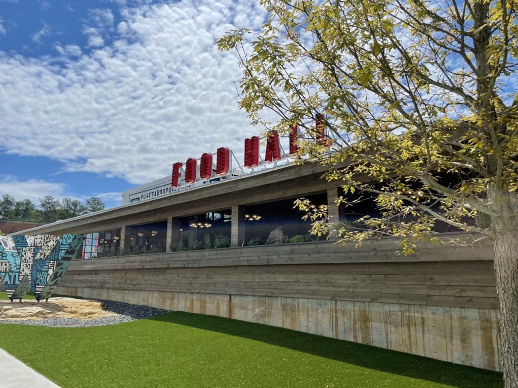 Outside in front of a small wood building with Food Hall sign. Grassy area in front.