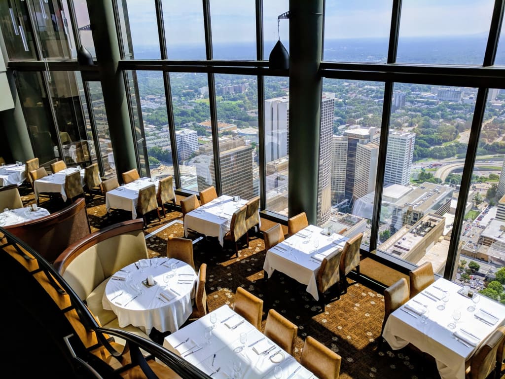 A modern restaurant with floor-to-ceiling windows overlooking a sprawling cityscape in Atlanta, Georgia.