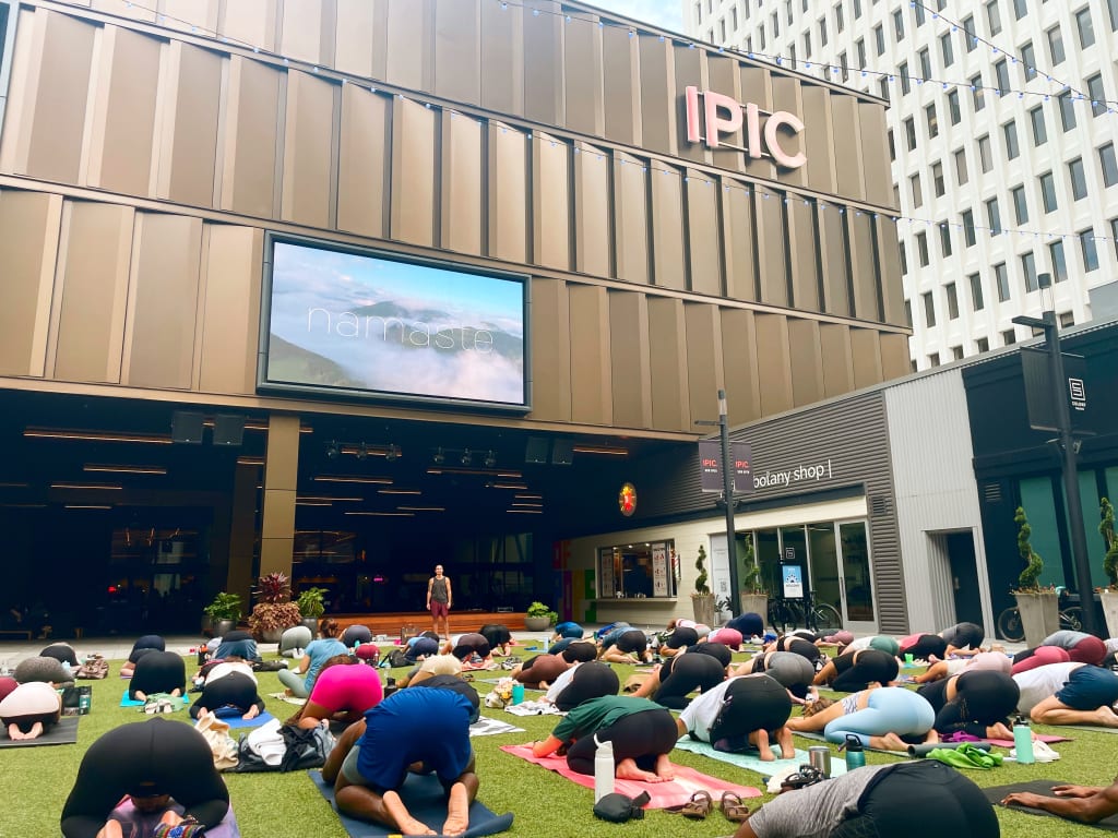 A large group of people practicing yoga outdoors on a grassy area in front of a modern building in Atlanta, Georgia.