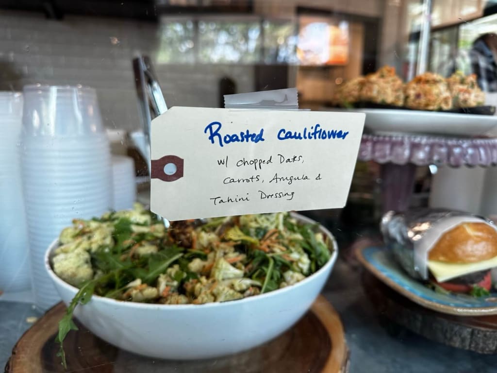 A white bowl of roasted cauliflower salad with oats, carrots, and tahini dressing on a wooden stand in Atlanta, Georgia.