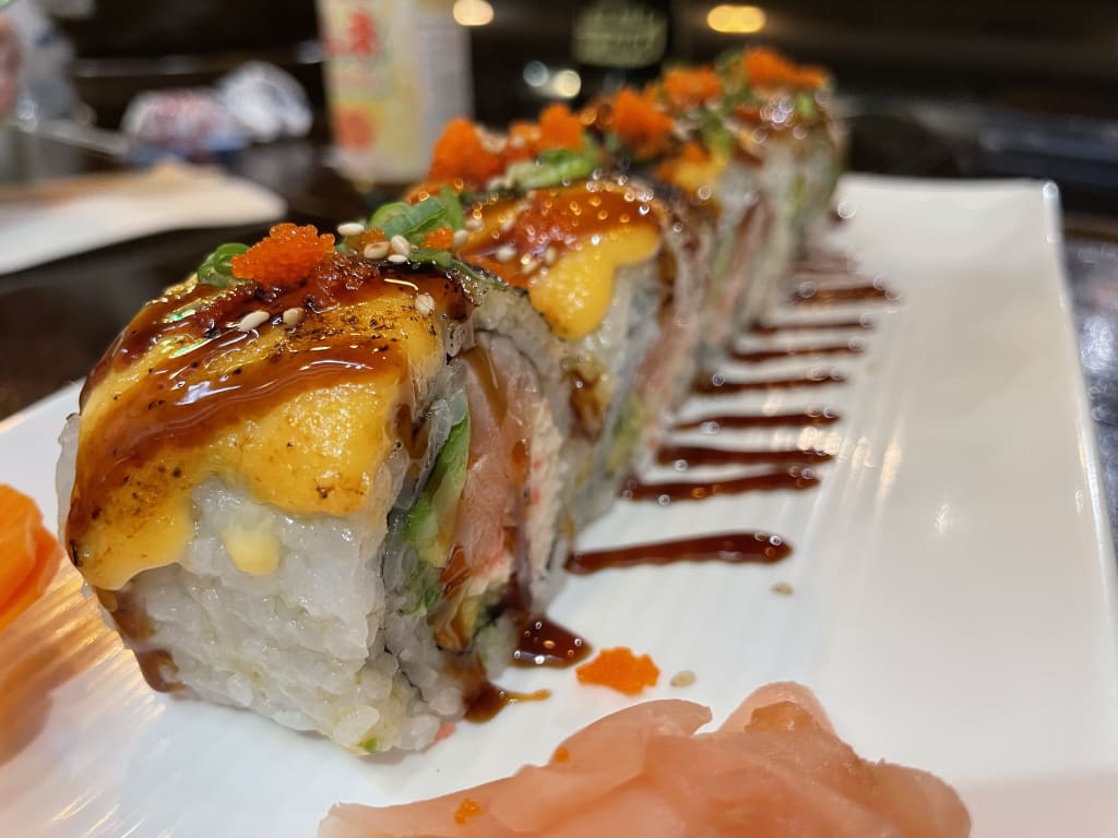 A plate of sushi rolls topped with orange tobiko and drizzled with spicy mayo and eel sauce in Atlanta, Georgia.