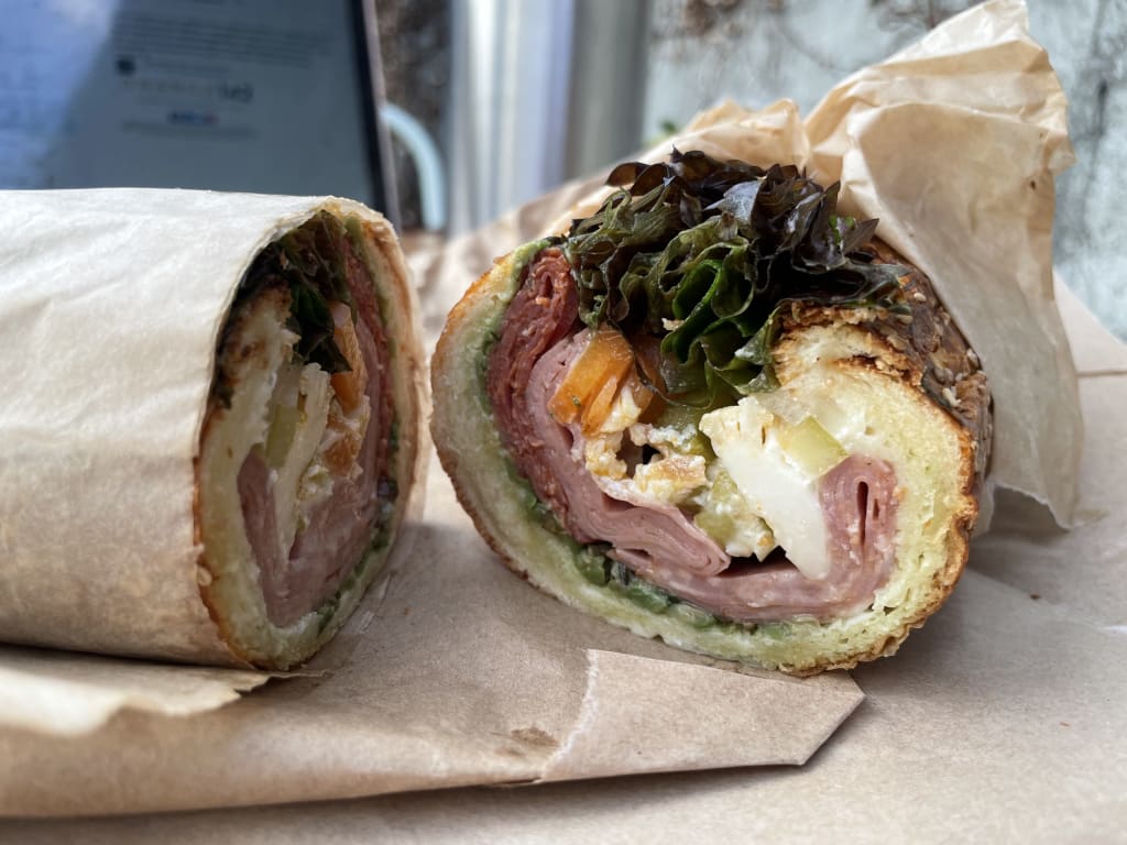 A freshly cut sandwich with ham, cheese, and greens wrapped in brown paper in Atlanta, Georgia.