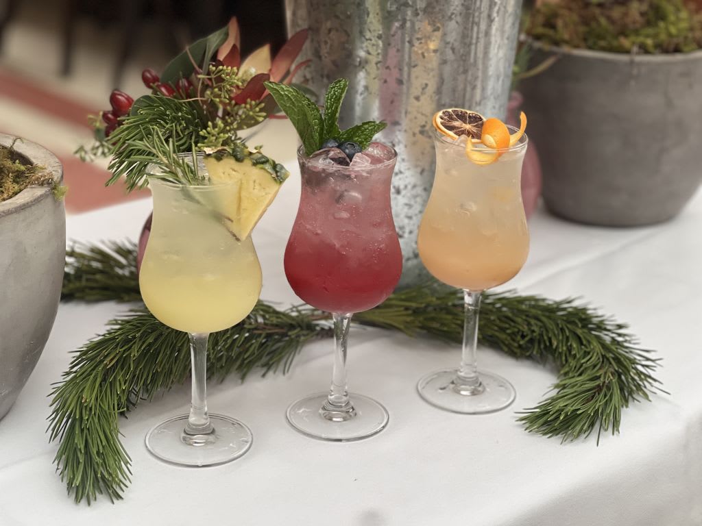 Three festive cocktails garnished with fruit and herbs in elegant glasses on a table in Atlanta, Georgia.