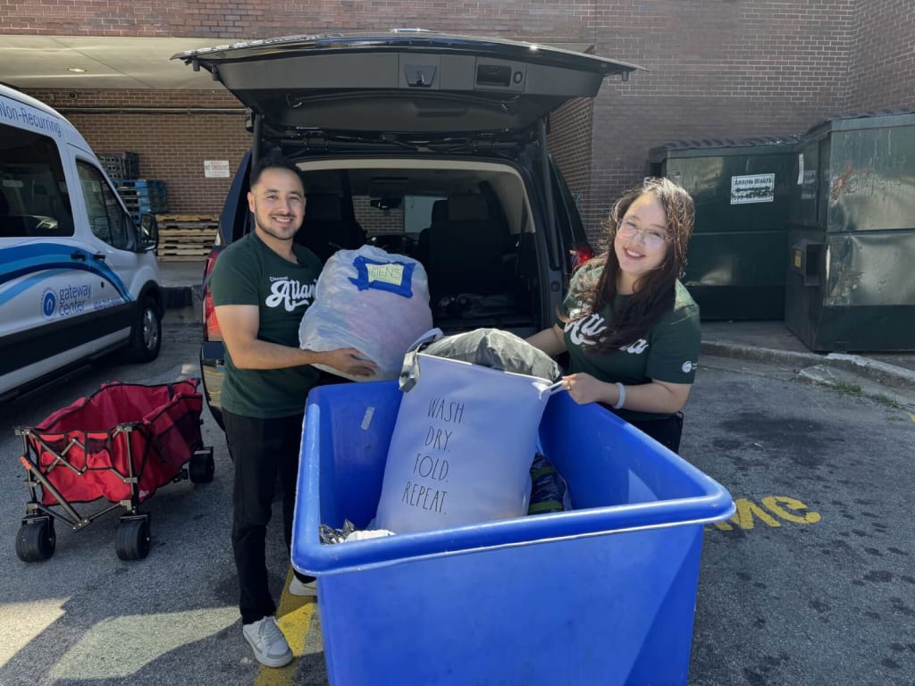 Two smiling volunteers load laundry bags into a blue bin behind a van in Atlanta, Georgia.