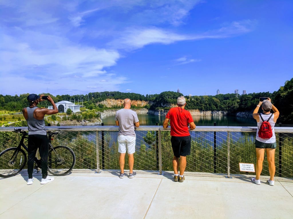 Four people stand on a bridge, taking photos of a scenic lake and forest view in Atlanta, Georgia.