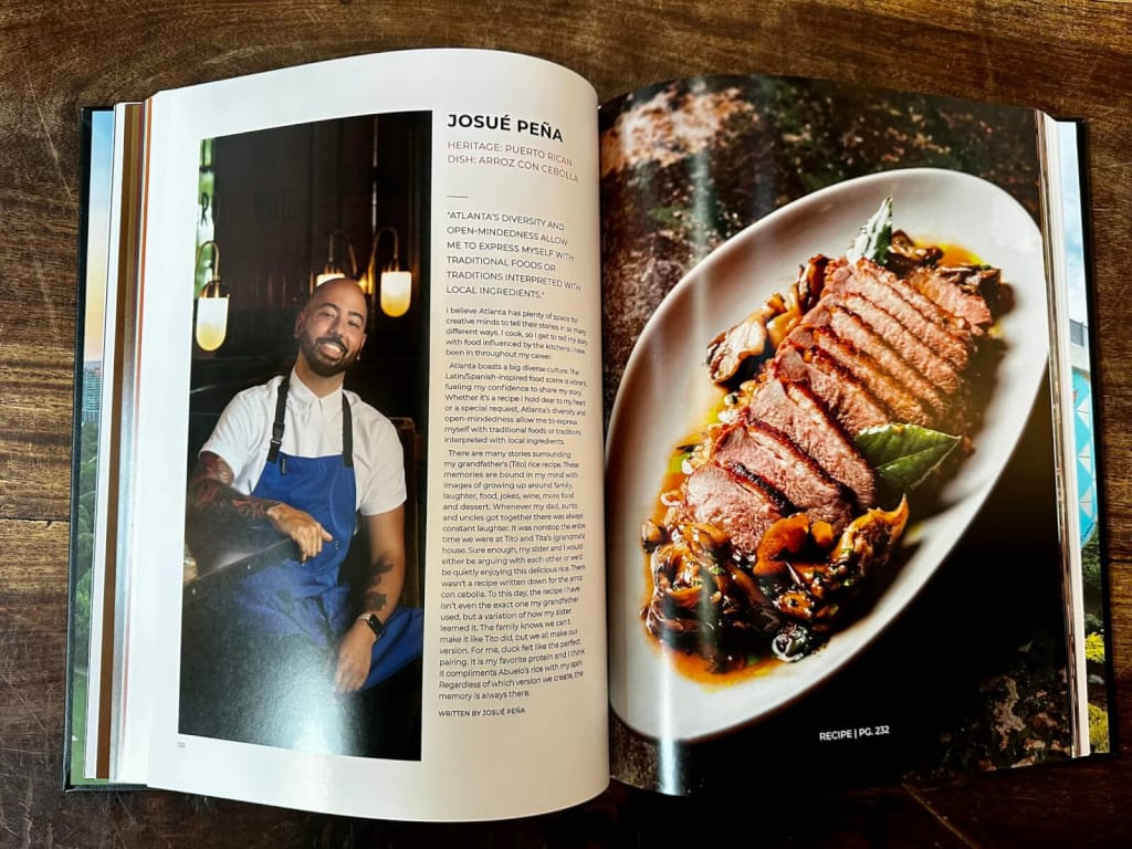 A chef in a blue apron sits next to a plate of sliced meat with mushrooms and greens in Atlanta, Georgia.