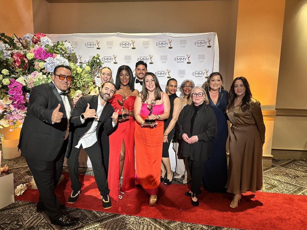 @DiscoverAtlanta Link In Bio 62 A diverse group of people in formal attire pose together on a red carpet with Emmy awards in Atlanta, Georgia.