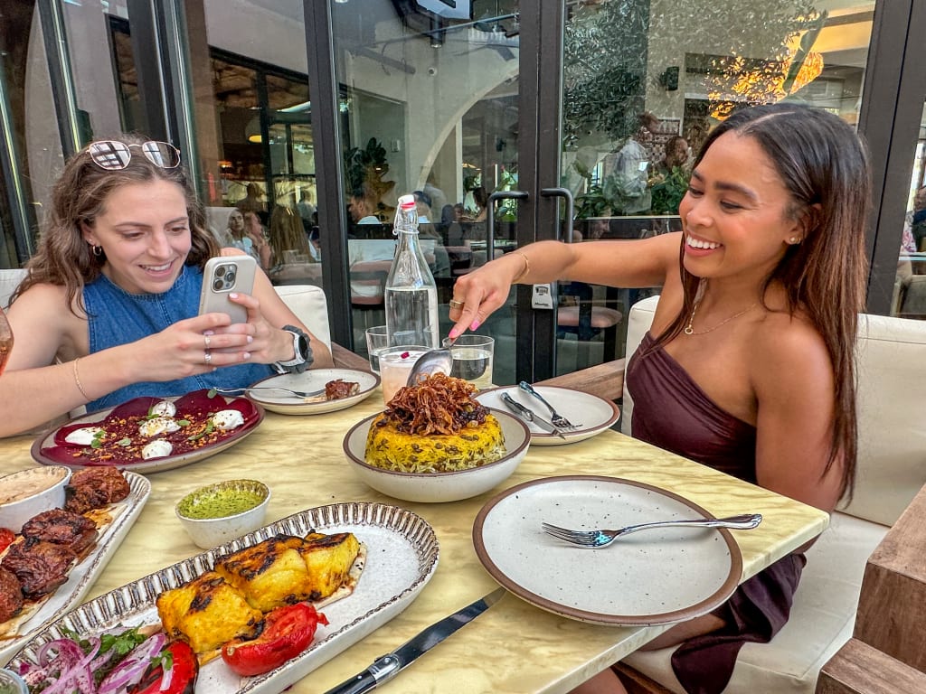 Two women enjoying a meal together at an outdoor restaurant, one taking a photo of the food in Atlanta, Georgia.