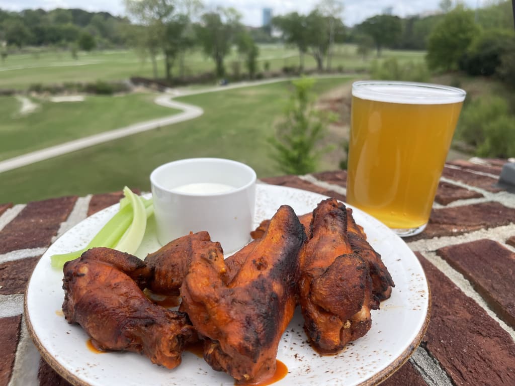 A plate of grilled chicken wings with celery sticks and ranch dip, accompanied by a glass of beer in Atlanta, Georgia.