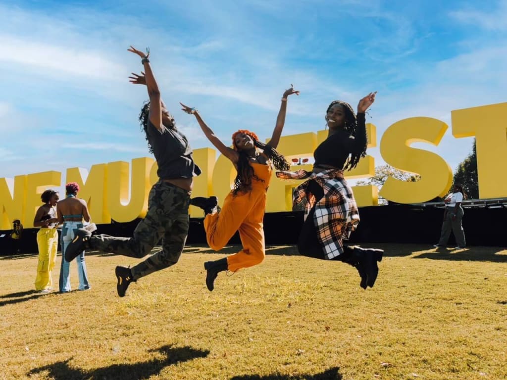 Three women joyfully leap in the air in front of a large yellow sign in Atlanta, Georgia.