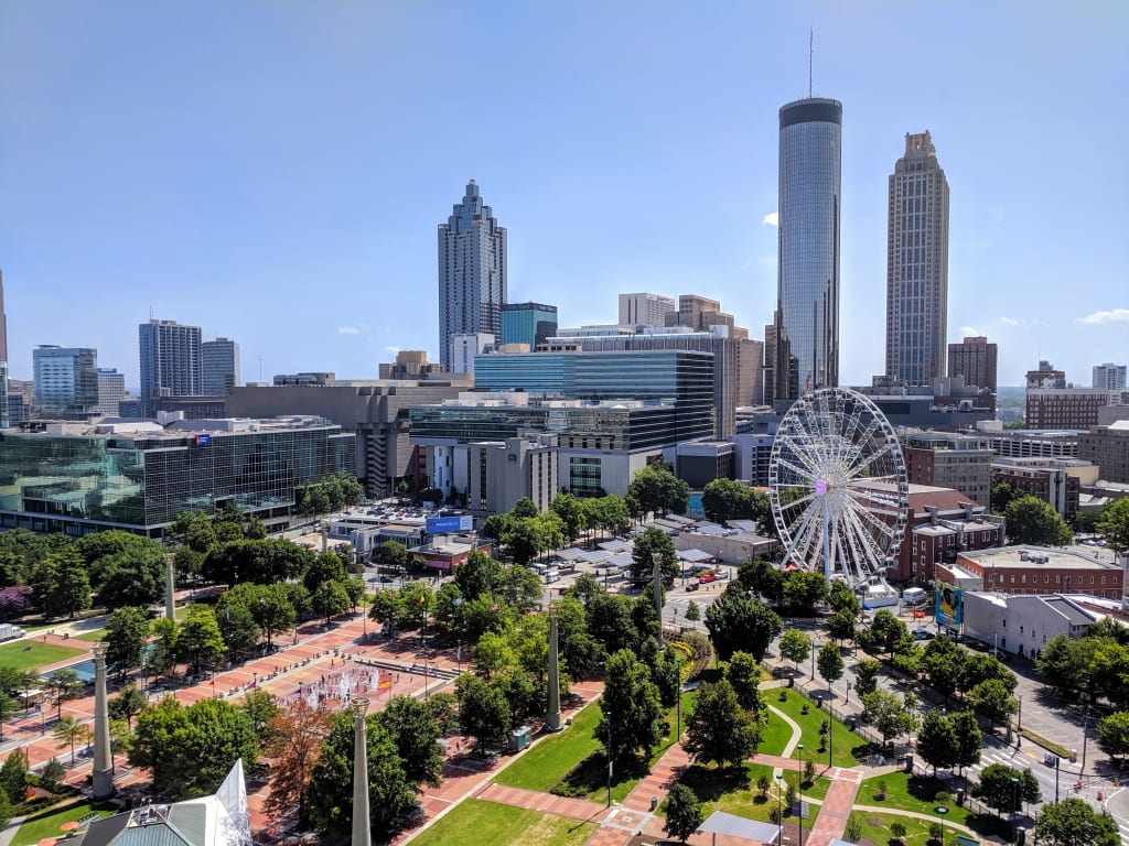 Aerial view of a bustling city with skyscrapers, a Ferris wheel, and a green park in Atlanta, Georgia.