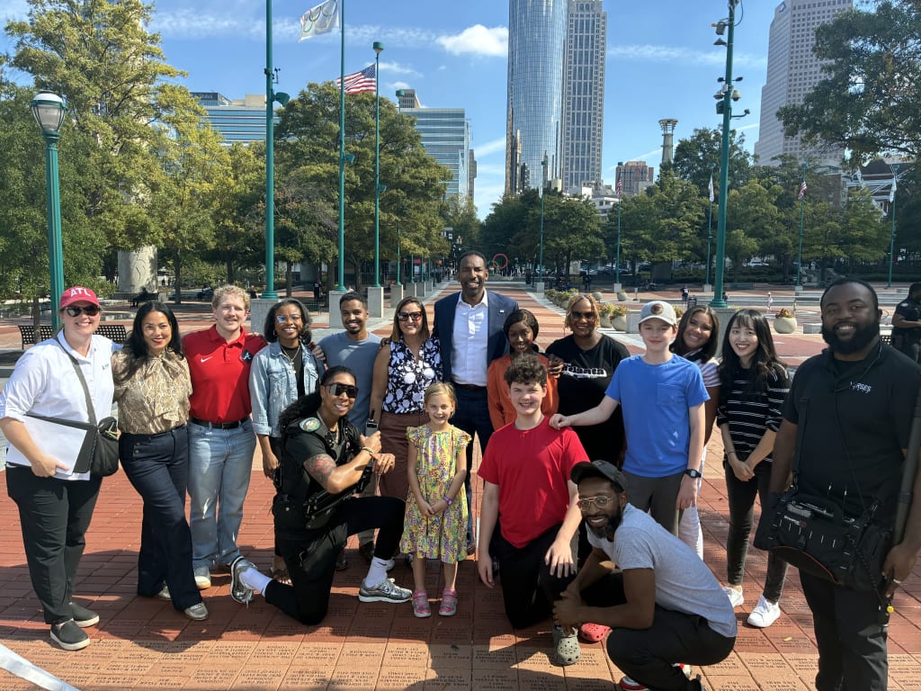 A diverse group of people, including children and police officers, pose together outdoors in a city park in Atlanta, Georgia.