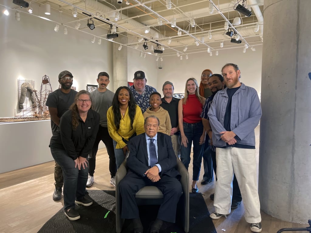 A diverse group of people, including an elderly man in a suit, pose for a photo in a modern art gallery in Atlanta, Georgia.
