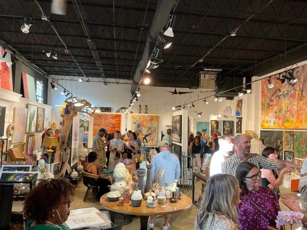 Crowded art gallery with paintings, sculptures, and people mingling in Atlanta, Georgia.