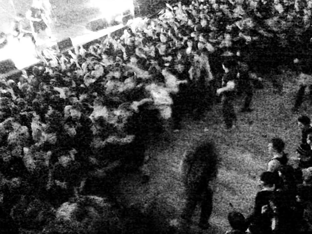 A black and white image captures a dense crowd of people at a concert, with some individuals raising their hands in excitement and others standing closely together, creating a sense of energy and movement in Atlanta, Georgia.