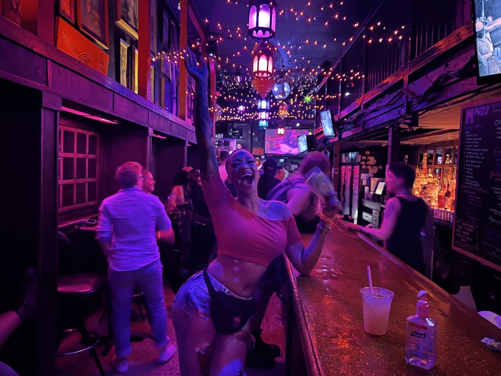 Woman standing at bar holding up a drink.