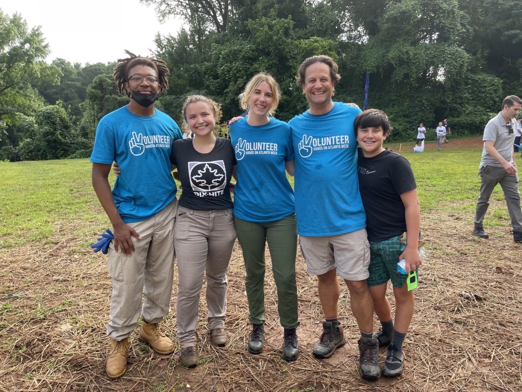 Five people posing for a picture together wearing volunteer shirts and standing in a garden.