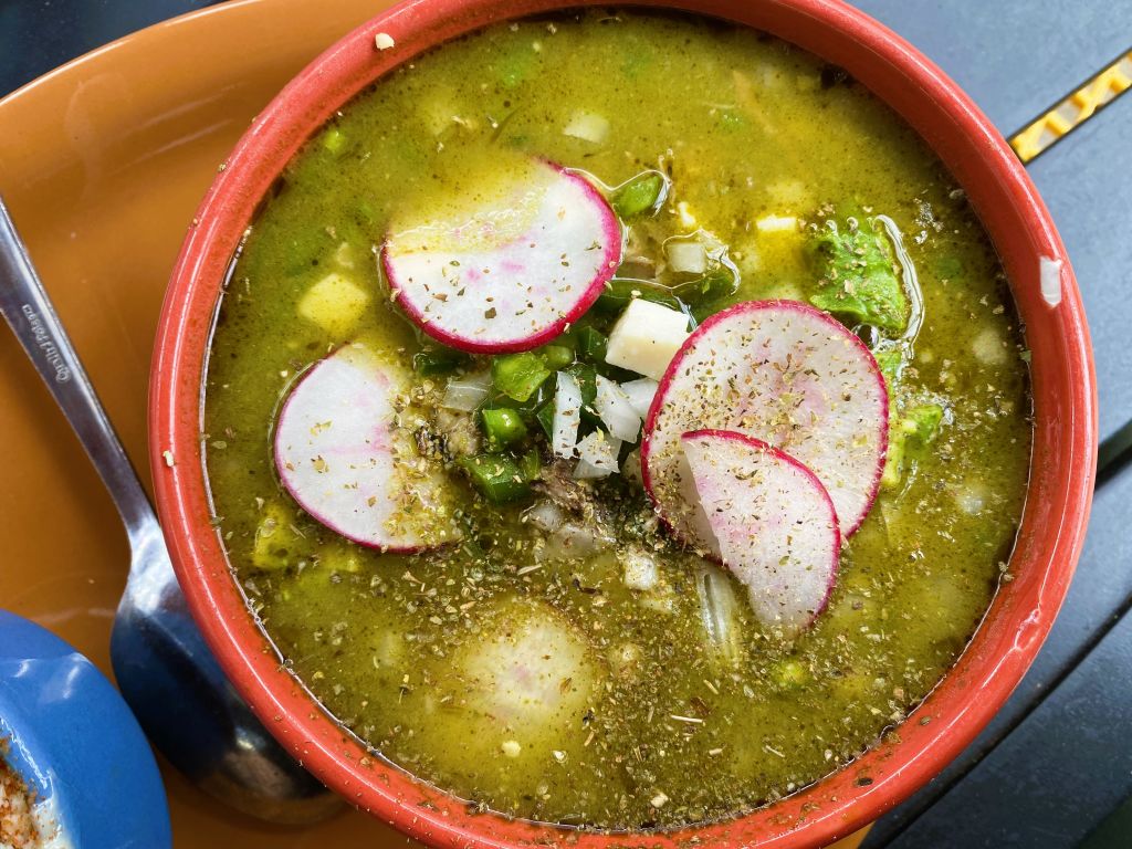 A vibrant green soup with radish slices, onions, and herbs in a red bowl in Atlanta, Georgia.