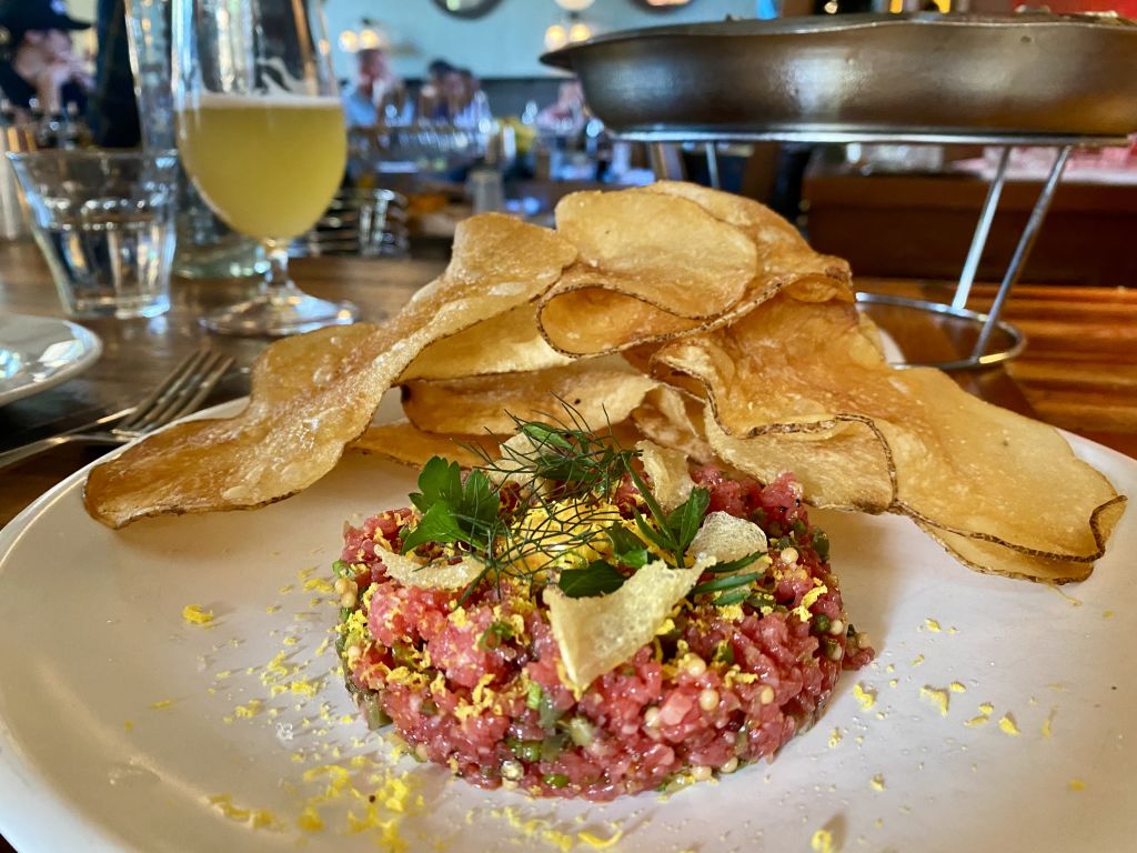 A plate with tuna tartare, crispy potato chips, and a glass of beer on a restaurant table in Atlanta, Georgia.