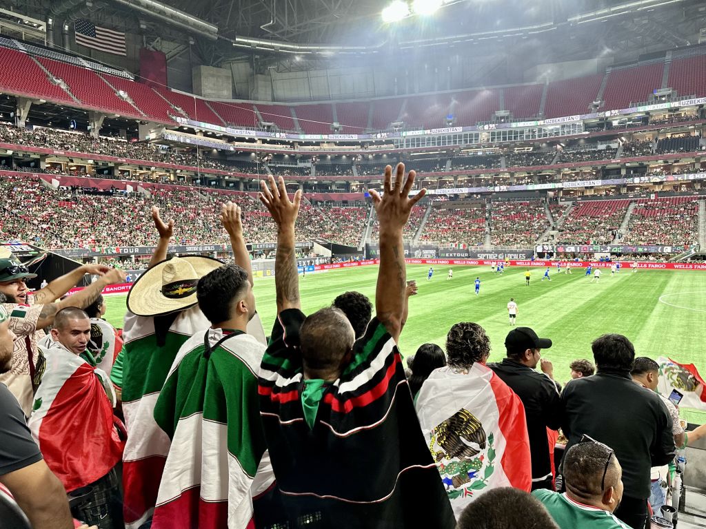Enthusiastic soccer fans in a packed stadium wave Mexican flags during a match in Atlanta, Georgia.