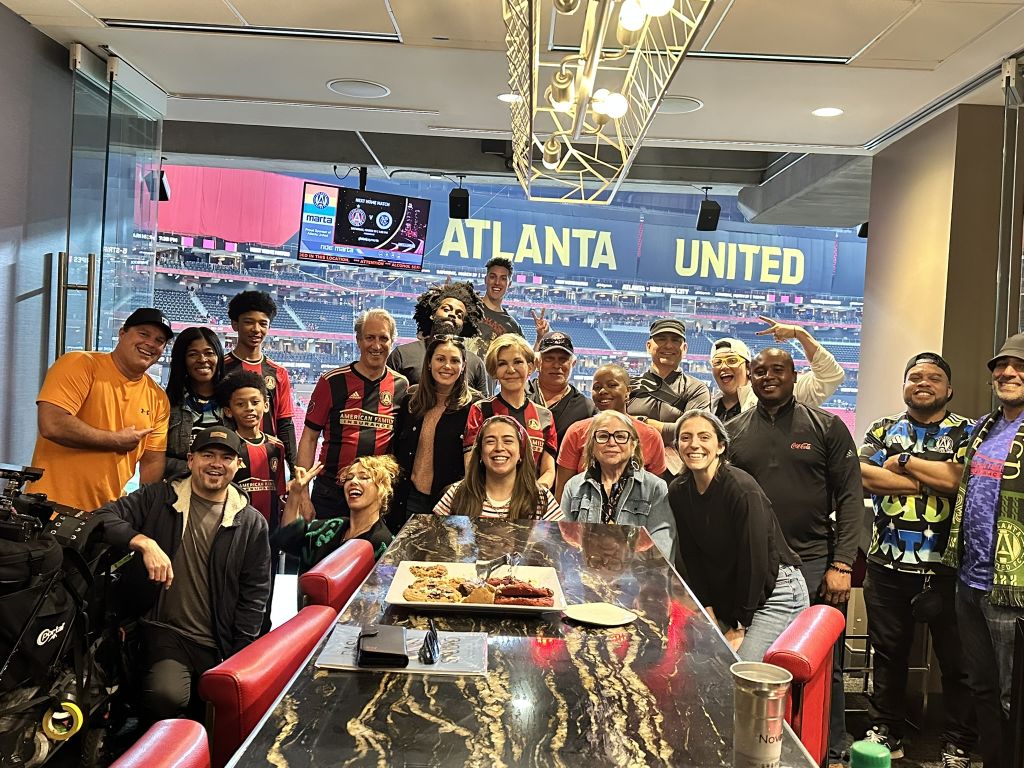 A diverse group of people, including children, celebrate together at a table with food and drinks in Atlanta, Georgia.