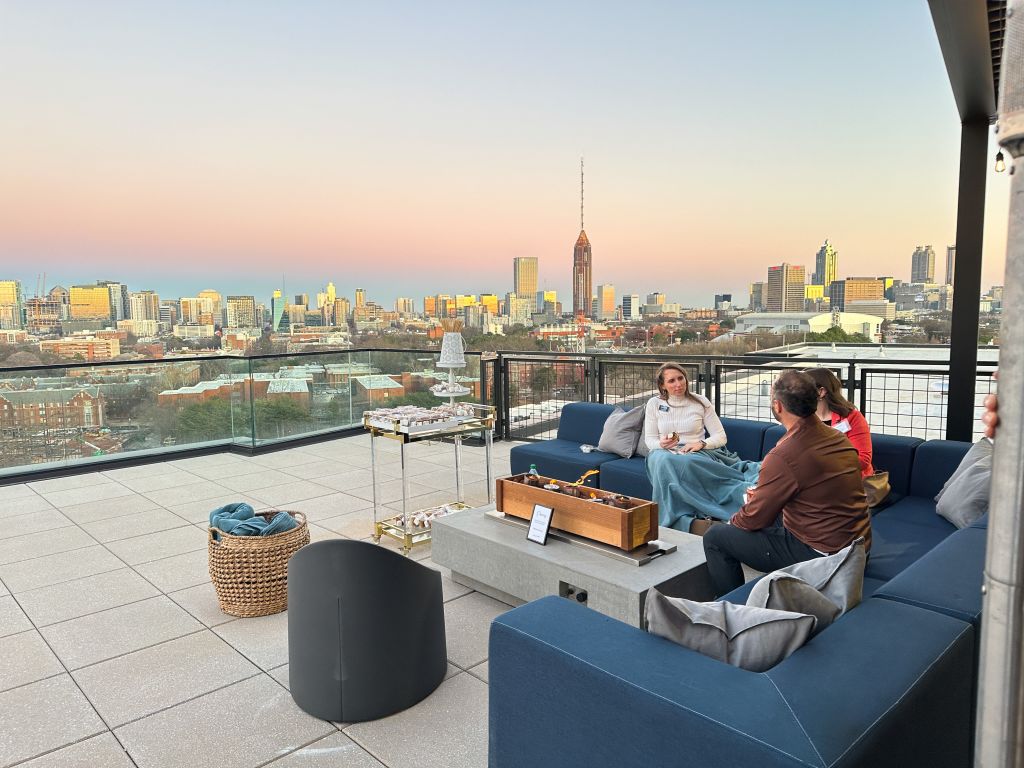 Three people relax on a rooftop patio at sunset, overlooking a city skyline in Atlanta, Georgia.