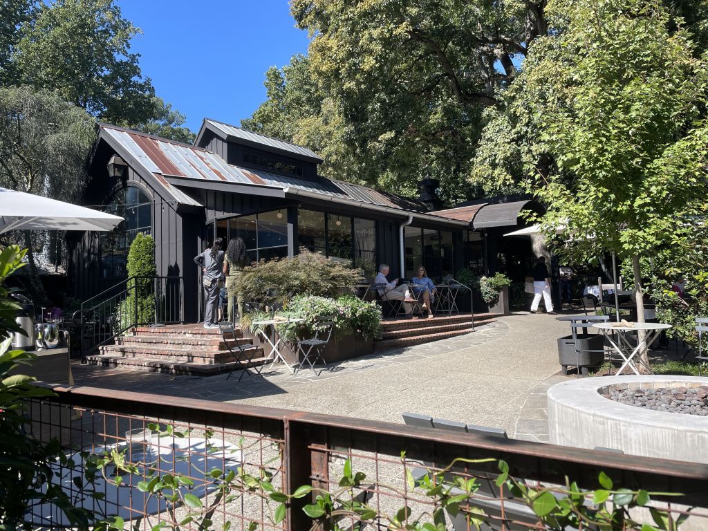A rustic outdoor restaurant with a black wooden building, surrounded by lush greenery and outdoor seating areas in Atlanta, Georgia.