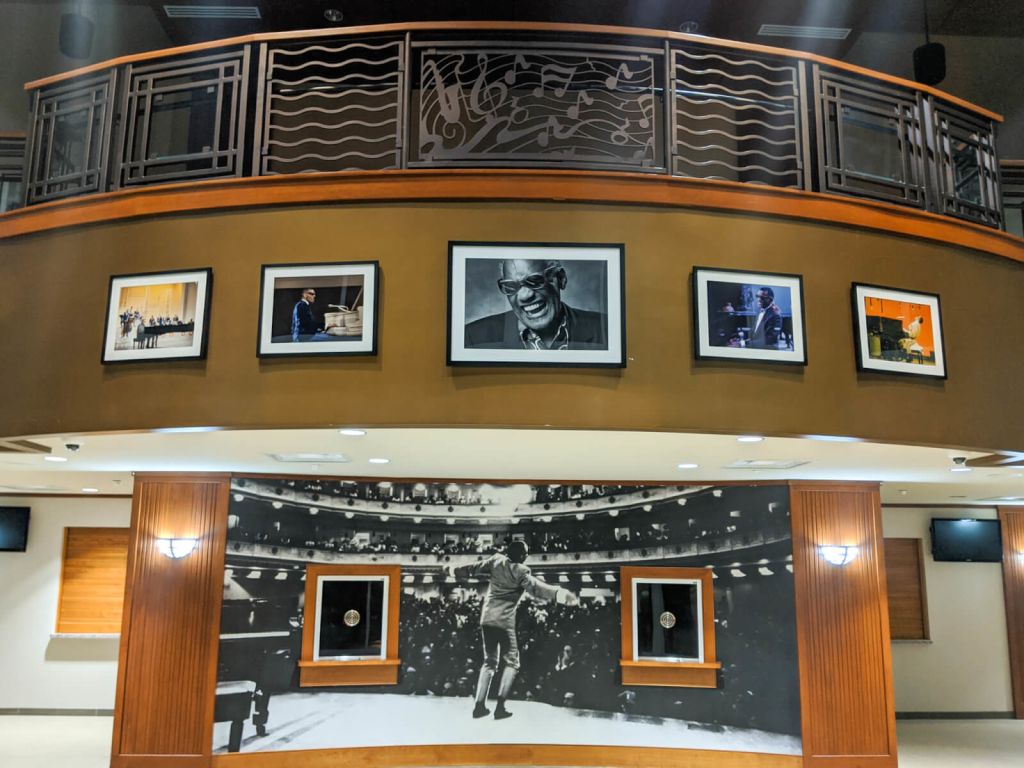 A grand, two-story lobby with a curved staircase, adorned with framed photographs and a large mural depicting a performer on stage in Atlanta, Georgia.