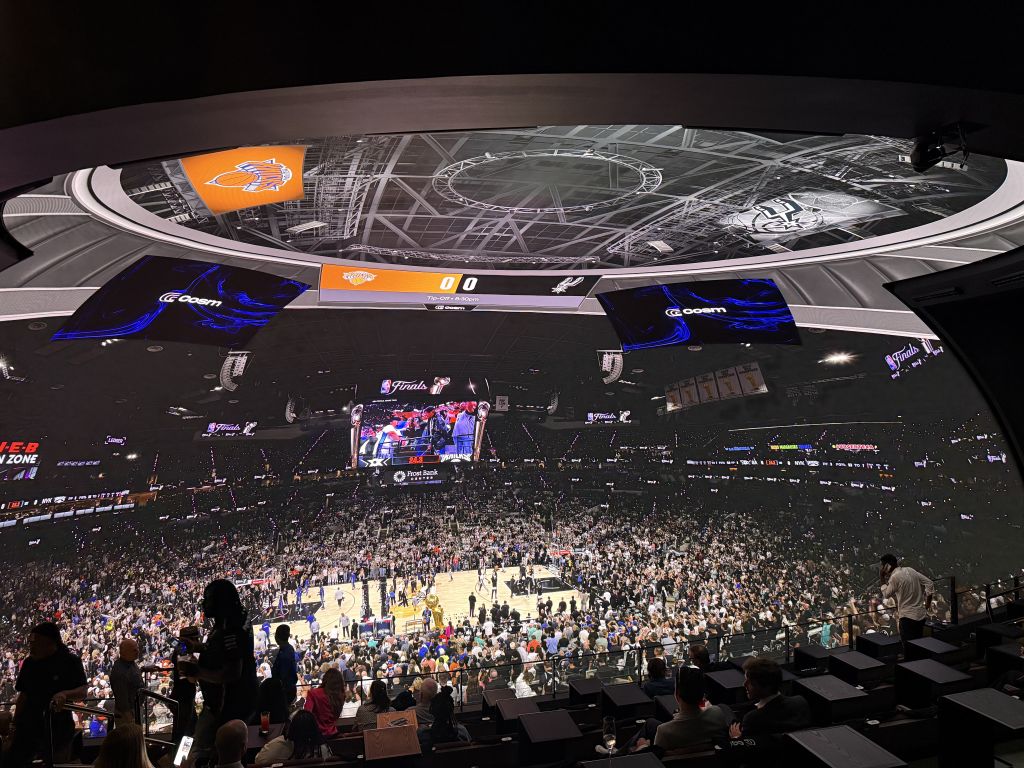 A packed basketball arena with a large crowd watching a game on a circular court below, surrounded by multiple levels of seating and large video screens in Atlanta, Georgia.