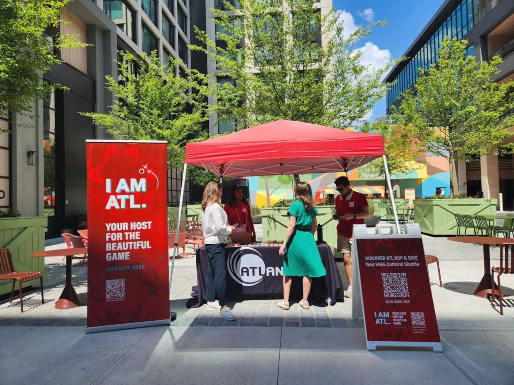 A promotional event for ATLANTA HOP & HIDE cultural shuttle under a red tent in an urban plaza in Atlanta, Georgia.